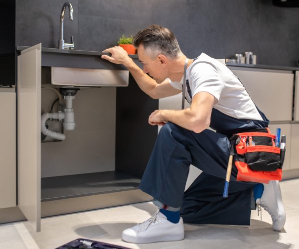 man-kneeling-down-touching-sink-inspecting-pipes (1)